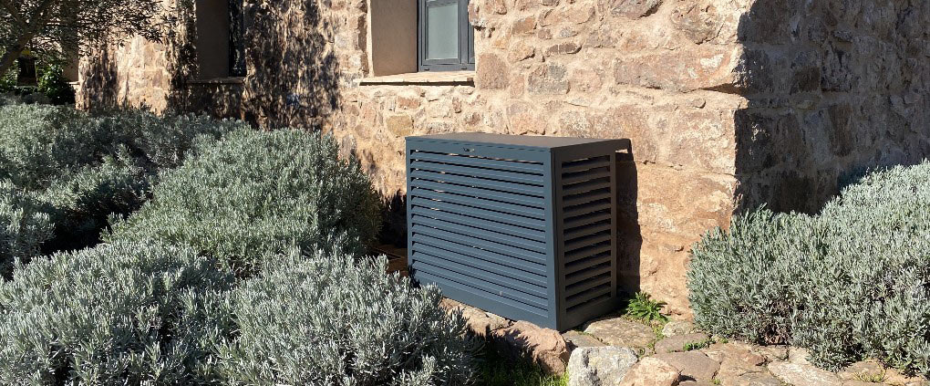 Cache noir de groupe extérieur de pompe à chaleur devant un mur en pierre naturel